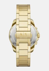 Kuldne roostevaba terasest kell link-käevõruga, A|X logo lukul ja läbipaistva tagaküljega. Omab ümarate servi ja poleeritud viimistlust.