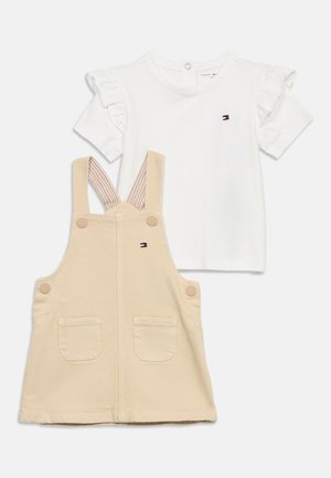 Completo composto da top bianco a maniche corte con volant e vestito salopette beige con tasche, con logo Tommy Hilfiger sul petto e sul davanti.