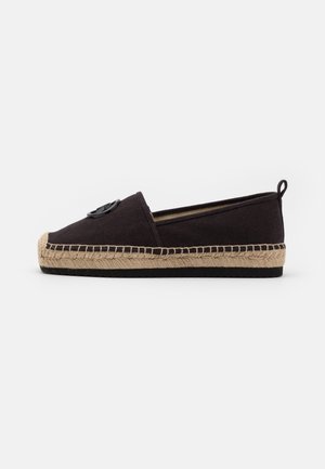 Sort lærred espadrille sko med vævet jutesål og sort cirkulært emblem på overdelen, set fra siden på en hvid baggrund.