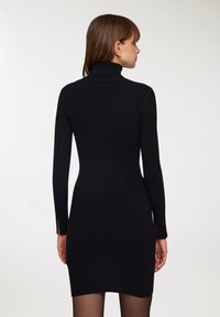 Czarna, prążkowana sukienka typu golf z długimi rękawami, dopasowanym krojem i detalem w postaci bocznego rozcięcia. Brak widocznych wzorów i elementów metalowych. Gładka tekstura.