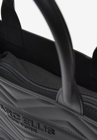 Borsa tote nera con una texture trapuntata, dotata di un compartimento con zip, manici robusti e brand embossato sul davanti.