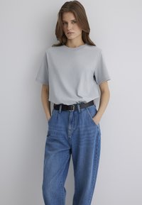 Light gray cotton t-shirt with short sleeves, paired with high-waisted blue denim jeans. Features a black belt with a buckle.