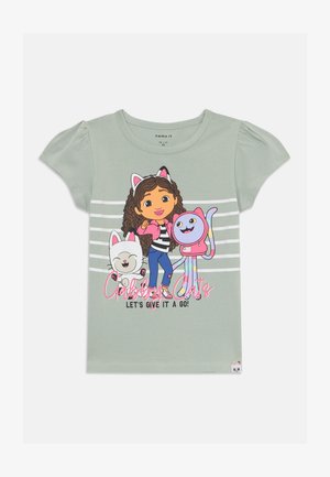 Camiseta de algodón verde claro con un personaje de cabello rizado marrón, orejas de gato y dos gatos de dibujos animados. El texto dice "¡Gatos Gruñones! ¡Vamos a intentarlo!"