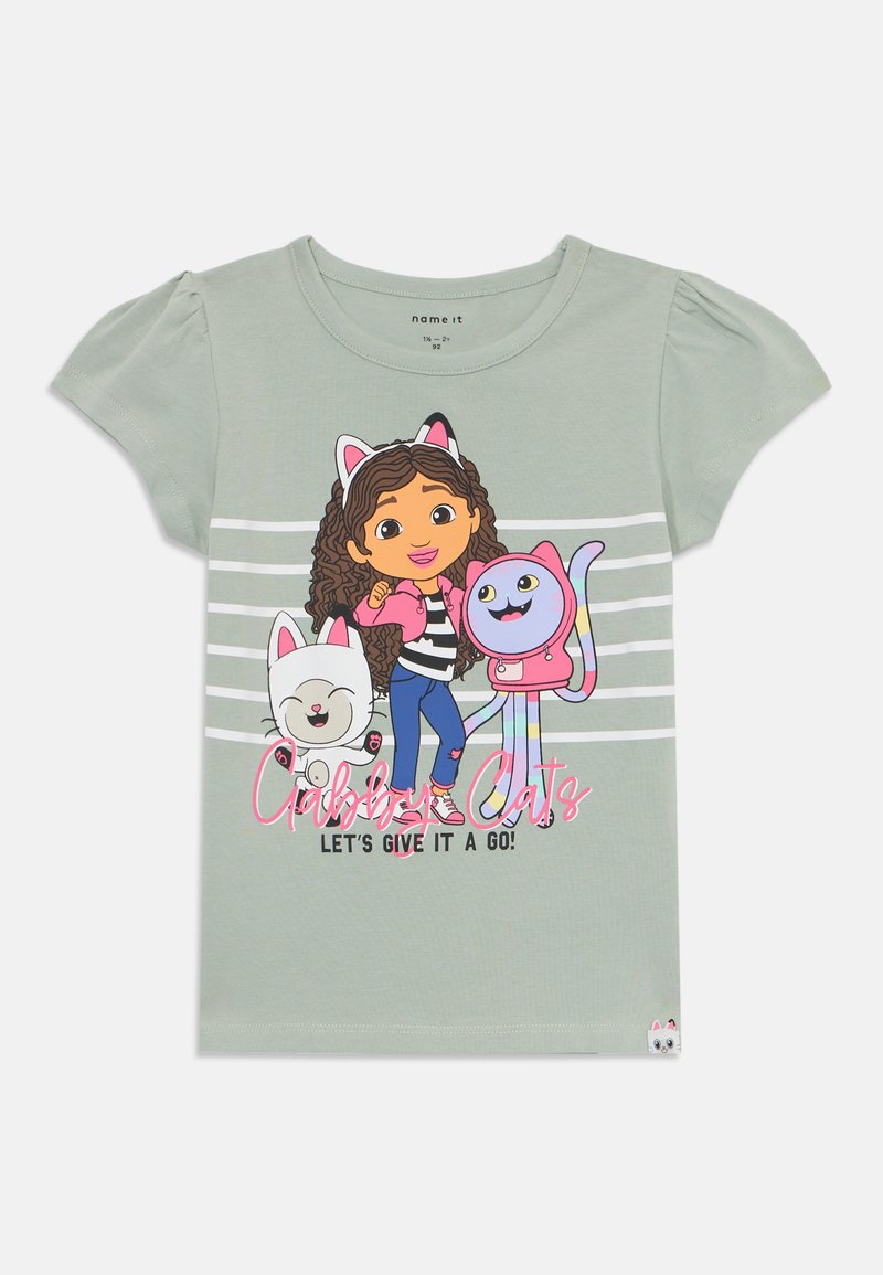 T-shirt de algodão verde claro com um personagem de cabelo castanho encaracolado, orelhas de gato e dois gatos de desenho animado. O texto diz "Gatos Murmuradores! Vamos experimentar!"