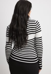 Black and white striped ribbed sweater with long sleeves, fitted design, and a round neckline, seen from the back. Textured fabric.