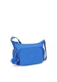 Blue crossbody bag with a textured fabric, zipper closure, front pocket, and a detachable fluffy charm. Features an embossed logo.