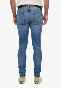 Vaqueros de denim azul claro con un corte ajustado, que cuentan con dos bolsillos traseros, un sutil efecto de desgaste y un parche de cuero marrón en la cintura.