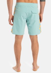 Svetlomodré plavky s oranžovým kockovaným vzorom na bokoch, s zadnou vreckom a elastickým pásom. Kraťasy sú dĺžky do polovice stehna.