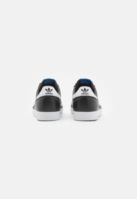 Ténis em preto e branco com parte superior em couro texturizado, sola em borracha branca e detalhes em azul no calcanhar e na língua. Logo da Adidas visível.