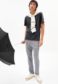 Black t-shirt, light-colored striped sweater draped on shoulders, gray striped pants, holding a black umbrella, white sneakers with beige accents.