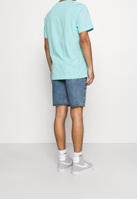 Turkos bomulls-T-shirt med korta ärmar, kombinerad med ljusblå denimshorts. Vita högstövlar med grå accenter och logotyp.