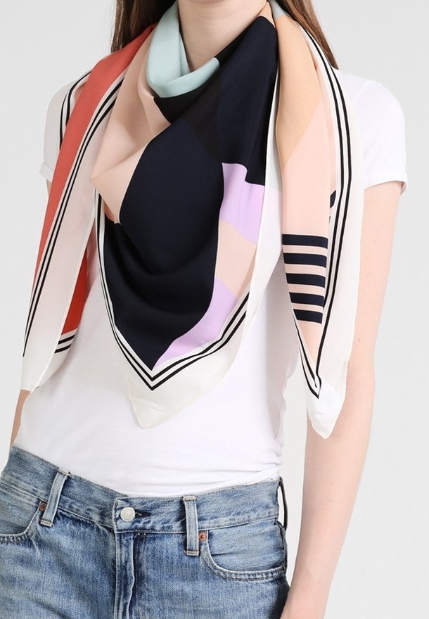 Écharpe à motifs géométriques noirs, pêche, lilas, sarcelle et corail, portée sur un t-shirt blanc et un jean bleu.