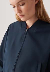 Giacca bomber blu navy con chiusura a zip, colletto a coste e finitura opaca. Presenta tasche laterali e una vestibilità comoda. Texture liscia e morbida.