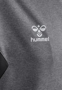 Grauer strukturierter Stoff mit einem Netzmuster; verfügt über ein weißes Logo und das Wort "hummel", das prominent auf der Oberfläche dargestellt ist.