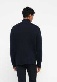 Sweater tricotado azul-marinho com colarinho alto, mangas longas e um corte descontraído, apresentando uma textura suave e uma bainha reta.