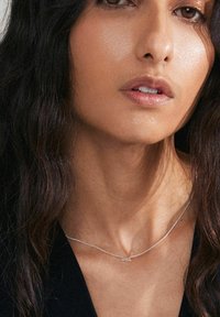 Silverhalsband med en delikat kedja som har ordet "love" i kursiv. Huden har en jämn struktur, mot en mörk topp.