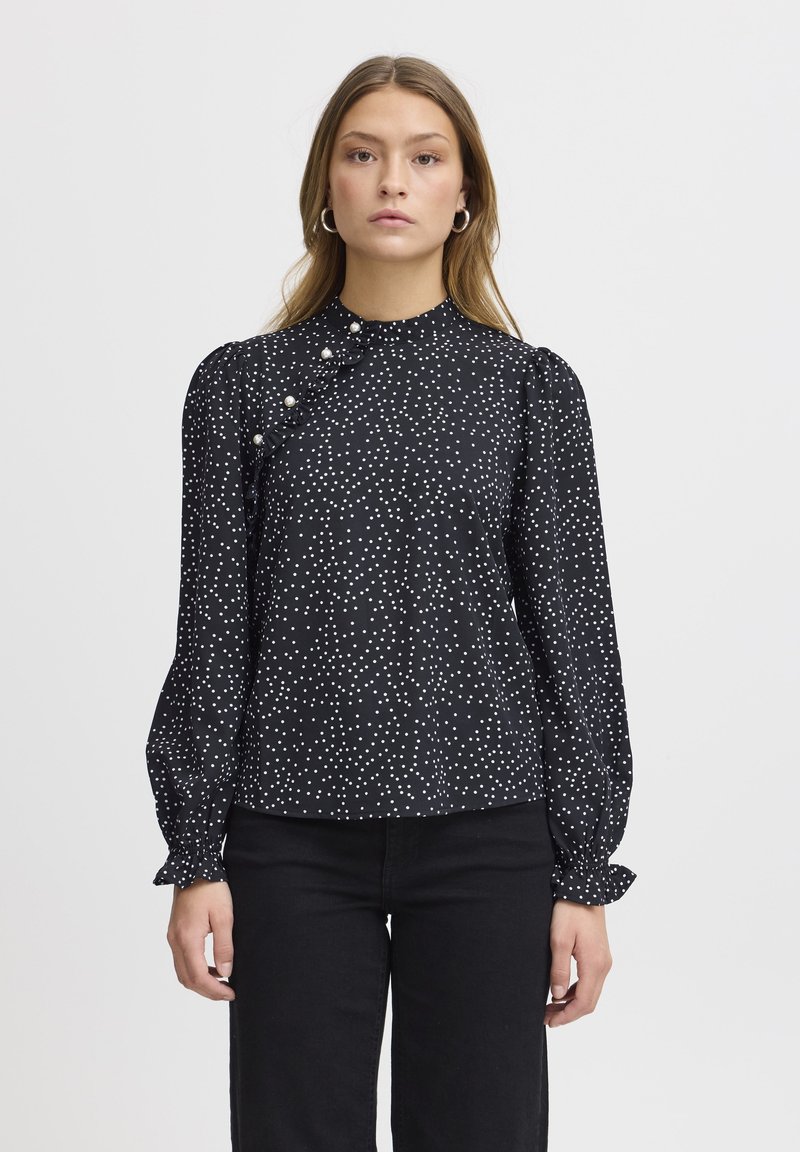 Blusa nera con pois bianchi, maniche lunghe a sbuffo, dettaglio frontale arricciato e bottoni decorativi. Tessuto liscio e vestibilità comoda.