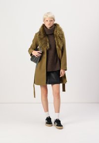 Olivengrøn frakke med faux fur krave, brun turtleneck og sort lædernederdel. Båret med sorte sneakers og hvide sokker.