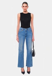 Black sleeveless bodysuit paired with high-waisted light blue flared jeans. The jeans feature a raw hem and slight fading. Black high heels and handbag.