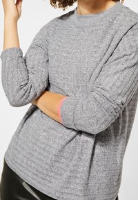 Haut en maille gris à manches longues avec motif texturé et encolure ronde. Présente des accents roses roulés aux poignets. Tissu doux.