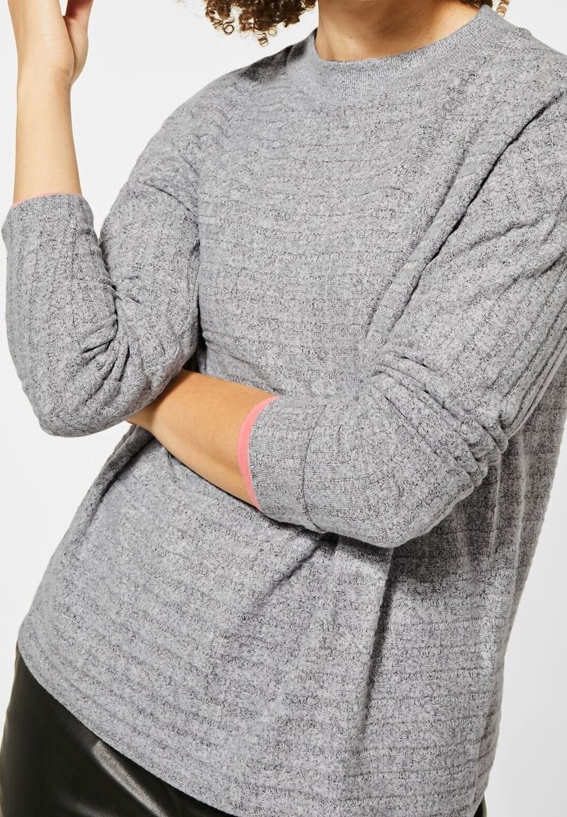 Haut en maille gris à manches longues avec motif texturé et encolure ronde. Présente des accents roses roulés aux poignets. Tissu doux.