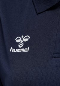 Donkerblauw stof met wit hummel-merklogo met een gestileerde bij boven de tekst op een poloshirt.