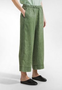 Zielone spodnie o szerokich nogawkach z teksturowanym wykończeniem, elastycznym pasem i kieszeniami. Połączone z prostymi czarnymi butami wsuwanymi.