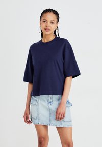 Mørkeblå cropped t-shirt lavet af bomuld, med korte ærmer. Sammen med en lys denimnederdel med to frontlommer.
