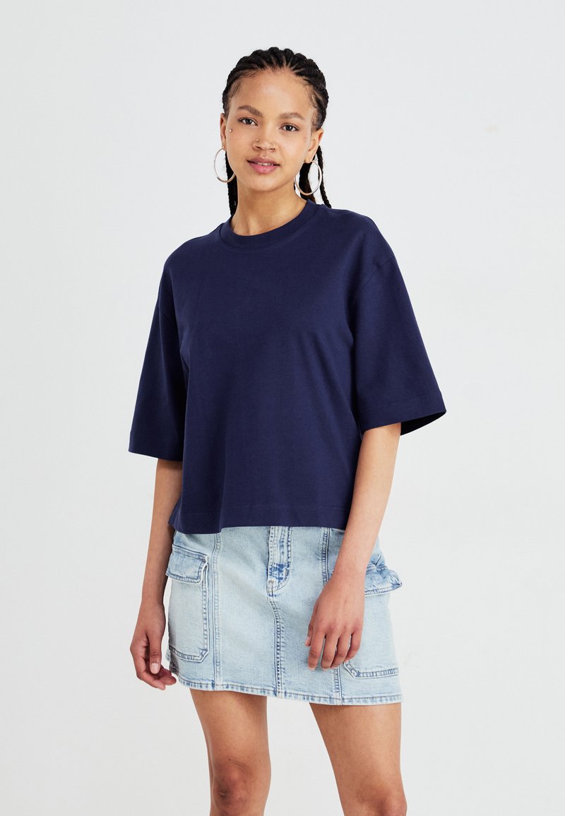 Mørkeblå cropped t-shirt lavet af bomuld, med korte ærmer. Sammen med en lys denimnederdel med to frontlommer.