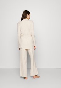 Beige loungewear set featuring a long-sleeve top with a cinched waist and wide-leg pants, made of soft, lightweight fabric.