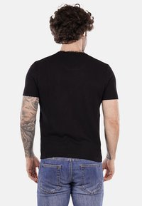 Camiseta negra de manga corta con una superficie texturizada, vista desde la parte de atrás, combinada con jeans de color azul claro. Presenta un escote redondo.