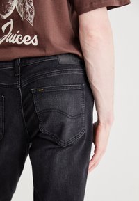 Black denim jeans with a classic design, featuring two back pockets and a leather label. The fabric has a slightly textured finish.