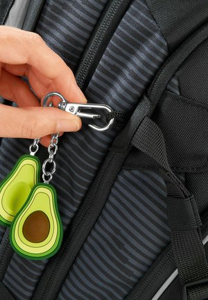 Schwarzer Rucksack mit gestreifter Textur, ausgestattet mit einem silbernen Metallclip und zwei grün-avocadoförmigen Schlüsselanhängern, die am Reißverschlusszieher befestigt sind.