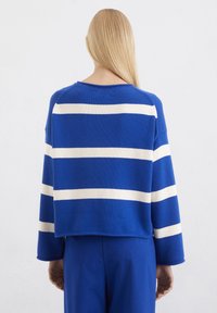 Blauer Strickpullover mit horizontalen weißen Streifen, weiten Ärmeln und rundem Ausschnitt. Texturierter Stoff, cropped Länge.