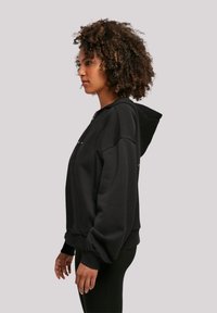 Black hooded sweatshirt featuring a zipper, wide sleeves, and ribbed cuffs. The fabric has a soft texture with a relaxed fit silhouette.