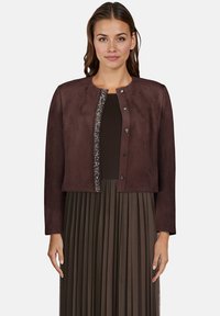 Brązowa skórzana kurtka w kroju cropped z okrągłym dekoltem, ozdobnym zapięciem na guziki oraz zdobioną koralikami przednią częścią. Pod spódnicą znajduje się plisowany materiał.