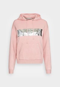 Felpa rosa con tasca frontale e lacci, caratterizzata da un logo "GUESS" argentato e lucido sul petto, su uno sfondo neutro.