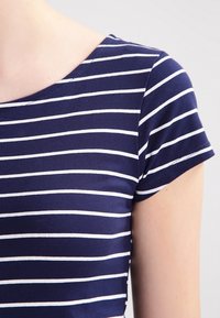 Mørkeblå T-shirt med vandrette hvide striber, rund halsudskæring, korte ærmer og en tætsiddende pasform. Glat bomuldsstof.