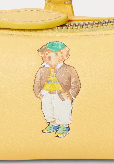 Yellow leather accessory with a printed cartoon bear wearing a green cap, brown jacket, yellow shirt, and beige pants, featuring colorful sneakers.