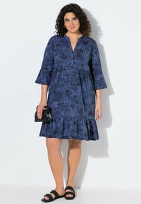 Vestito blu navy con stampa di motivi, scollo a V, dettagli con bottoni, maniche a tre quarti e orlo arricciato. Borsa nera e sandali.