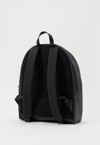 Black backpack with padded mesh straps, rounded shape, smooth synthetic material, and a subtle embossed design on the back.