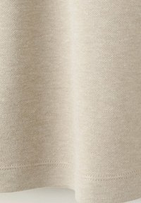 Gros plan d'un tissu tricoté beige avec une texture subtile et un ourlet cousu en bas.