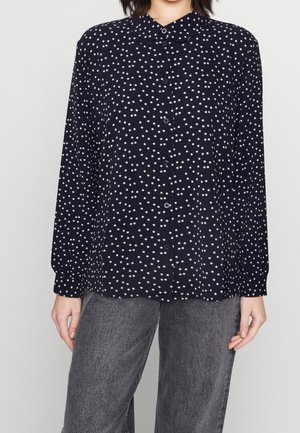 Chemise bleu marine à boutons avec des pois blancs, design à col, manches longues et coupe décontractée. Le tissu semble léger et texturé.
