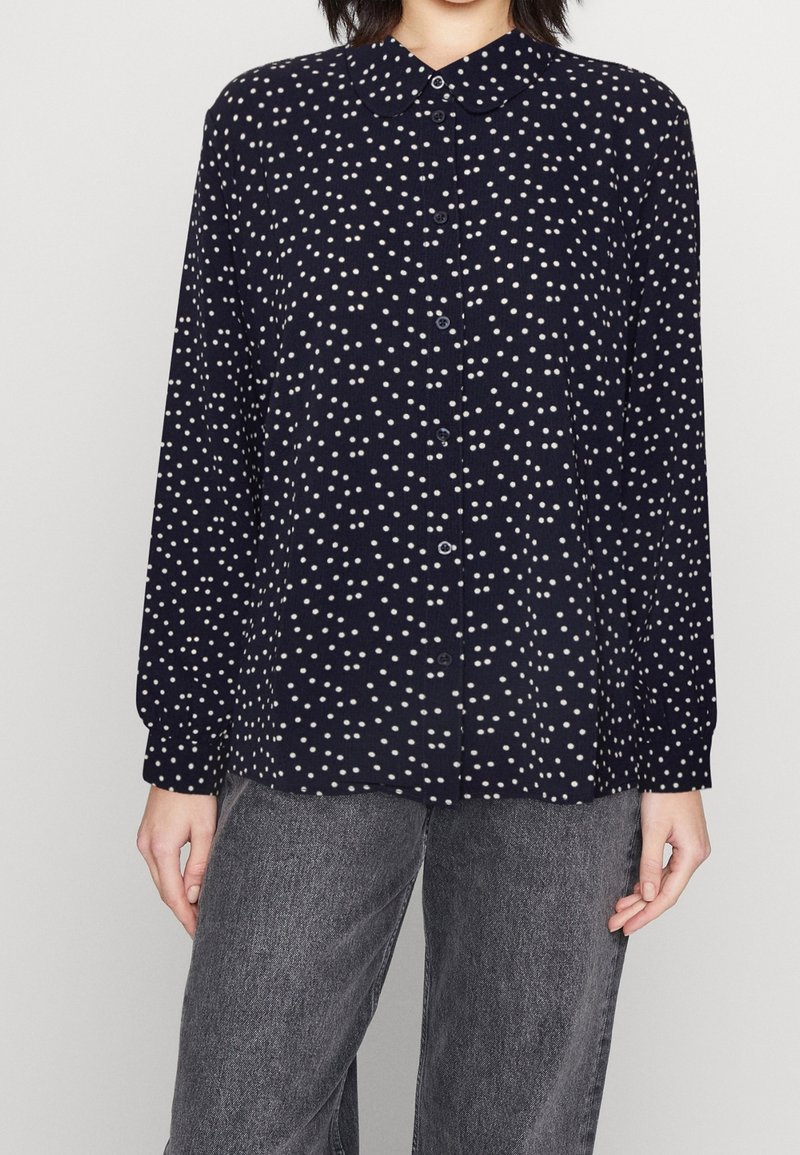 Navy button-up shirt with white polka dots, collared design, long sleeves, and a relaxed fit. Fabric appears lightweight and textured.