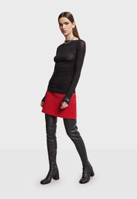 Zwarte lange mouwen top met geplooide textuur, rode mini-jurk en zwarte hoge hakken. Zilveren kettinghalsketting accentueert de ronde hals.