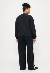 Sweat-shirt noir à coupe décontractée, avec des poignets et un ourlet côtelés. Associe à un pantalon noir avec des rayures blanches sur les côtés. Texture lisse.