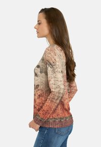 Camiseta de manga larga con un tejido texturizado que presenta un patrón de múltiples tonos en beige, óxido y marrón oscuro, acentuada con un dobladillo a cuadros.