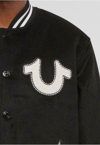Musterniga mustang jacket, millelt uhke tikandiga logo, nööbid ja triibulised ribatänavakraed ja varrukate aktsendid. Pehme tekstuur.