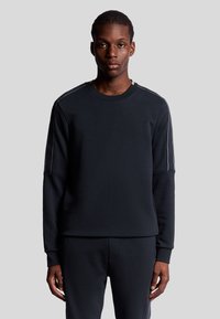 Felpa nera in tessuto morbido con maniche lunghe, caratterizzata da strisce bianche a contrasto lungo le cuciture delle spalle e un collo a giro.