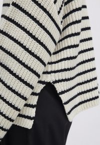 Strickpullover mit lockerer Passform, der cremige und schwarze horizontale Streifen, ein strukturiertes Muster und seitliche Schlitze am Saum aufweist.